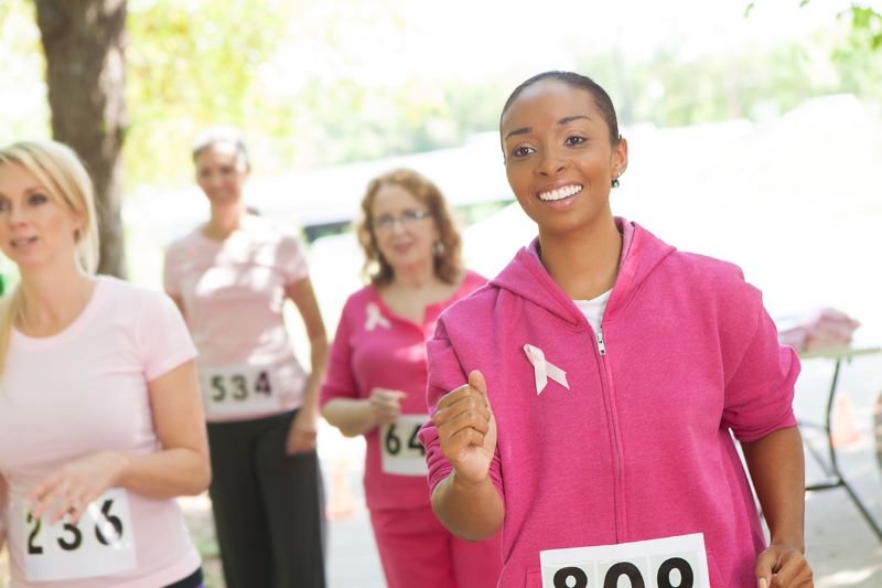 African American female wearing a dark pink zip up jacket and breast cancer ribbon pin is walking in a marathon
